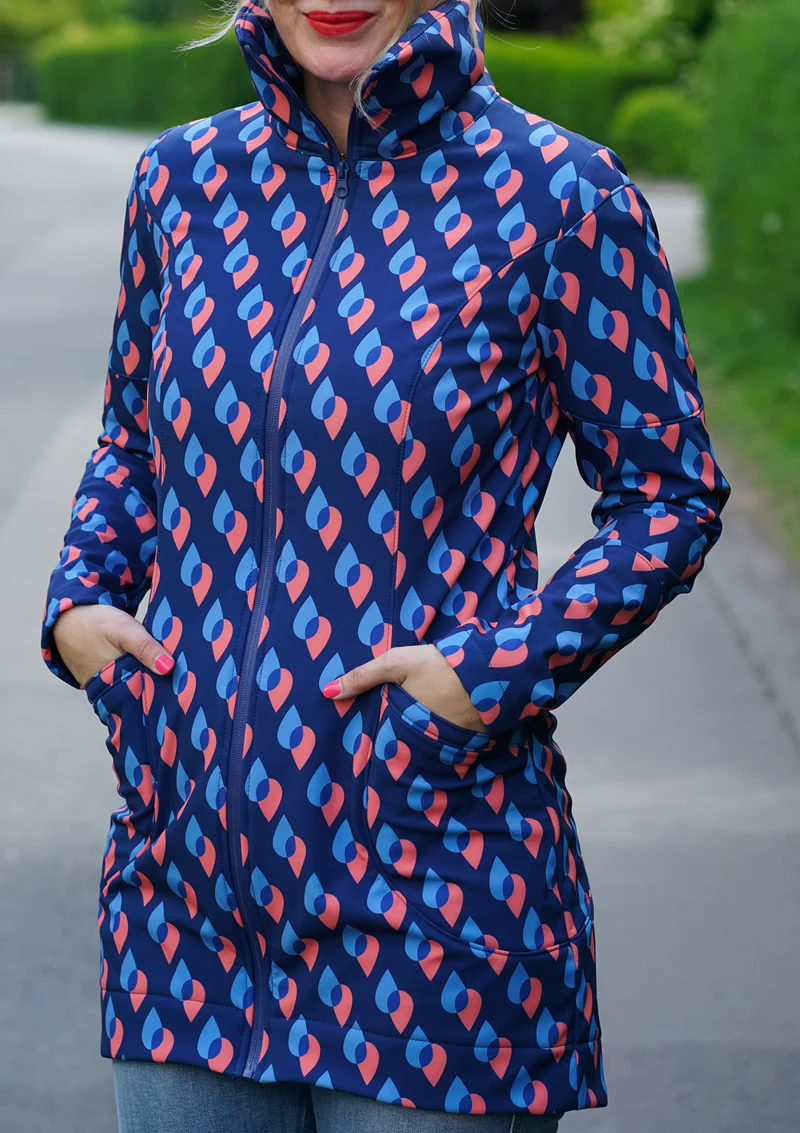 Navy jacket with pink and light-blue teardrop pattern, zipper front, hands in pockets, outdoors on a path.
