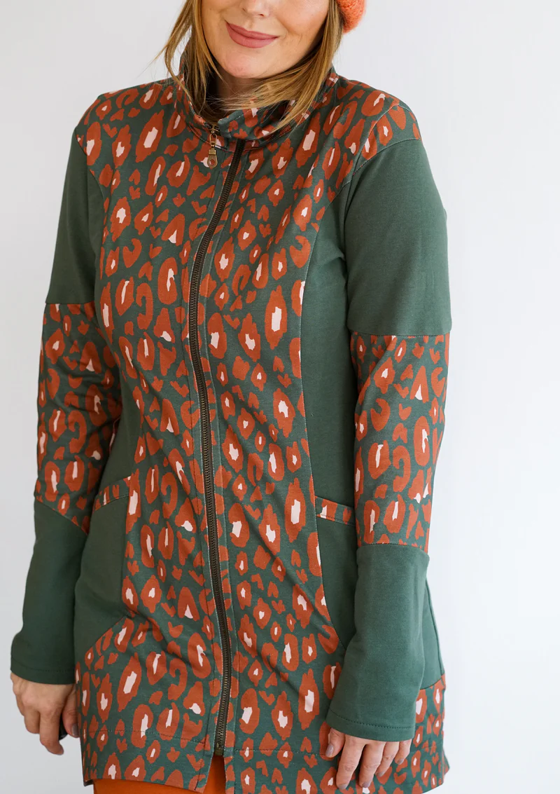 Woman modeling a dark green zip-up jacket with bold orange leopard-print panels on the front and sleeves.