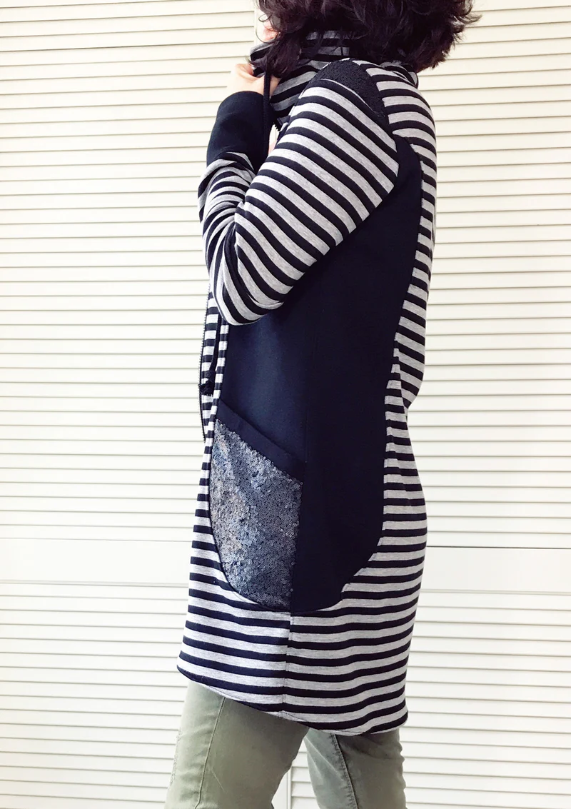 Side view of a person wearing a black-and-white striped cardigan with a large black panel and a sparkly sequin pocket, standing against a light background.