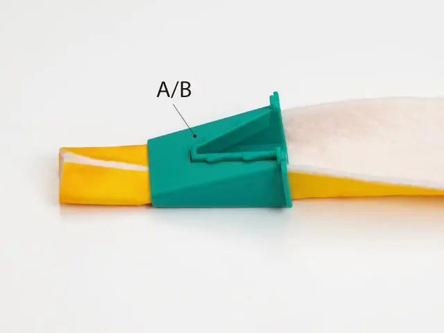 Close-up of a turquoise finger-prick device clipped to a finger, with 'A/B' labeled on the device — used for blood sampling.