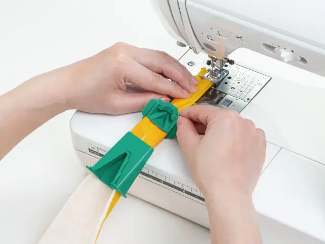 Person guiding yellow fabric through a sewing machine while a green fabric clamp holds pieces together.