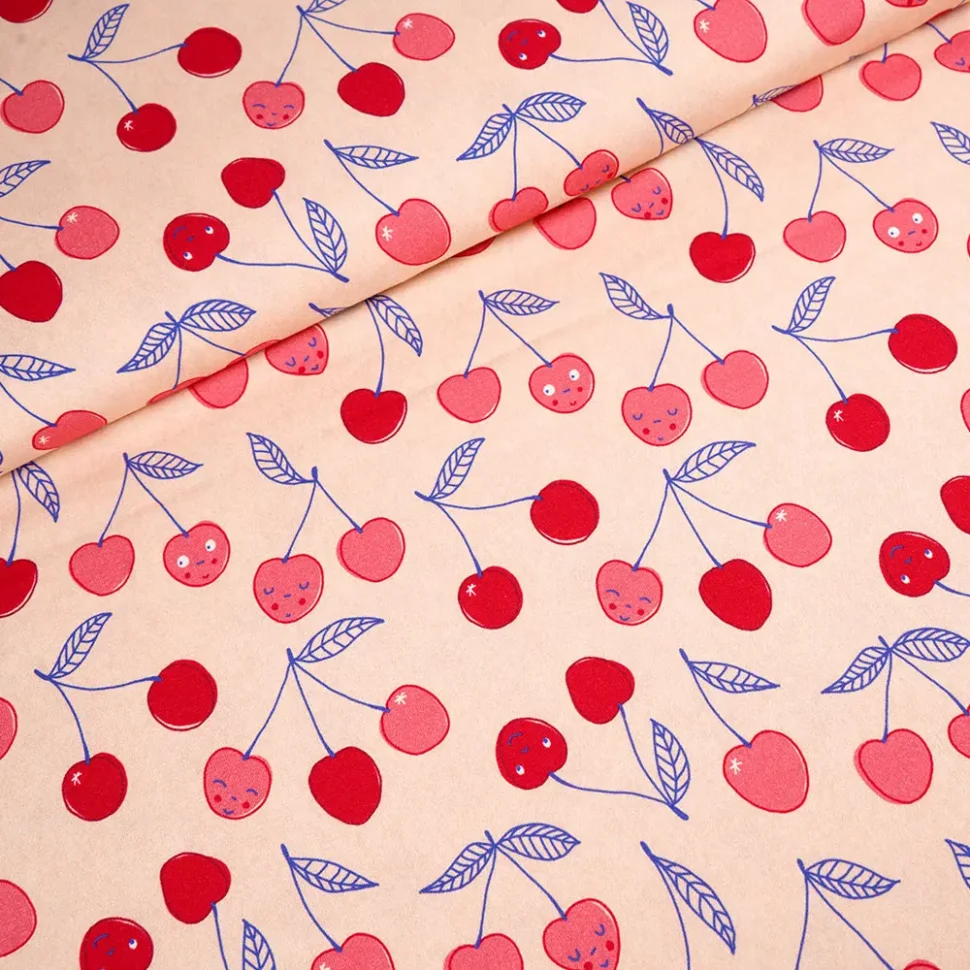 Beige fabric pattern with pink and red cherries and blue leaves scattered across, with gentle fold lines suggesting a draped textile.